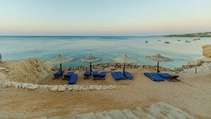 A beach with sun loungers and umbrellas, a clear view of the sea, and a rocky shoreline. - Siva Sharm Resort & Spa  (Sharm El Sheikh)