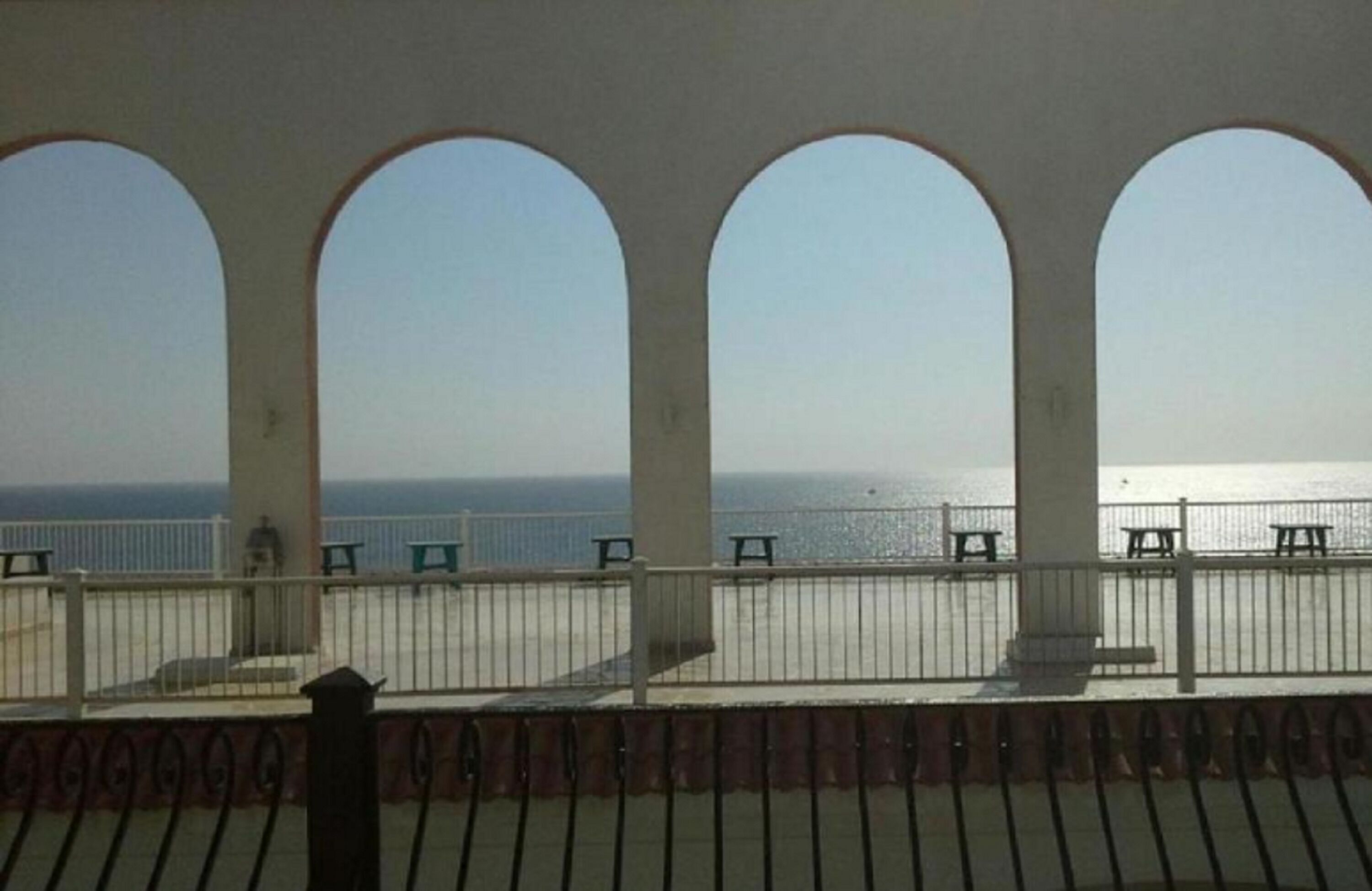 A balcony with a view of the sea, featuring a railing and benches.