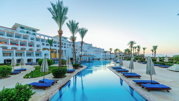 A hotel with a swimming pool, palm trees, and lounge chairs. - Siva Sharm Resort & Spa  (Sharm El Sheikh)