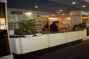 A hotel reception area with a reception desk, a digital clock, and a potted plant. - Monaco Quisisana (Jesolo)