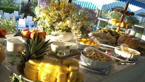 A buffet table with various fruits, vegetables, and a flower arrangement. - Monaco Quisisana (Jesolo)