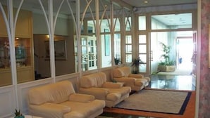 A spacious living area with a beige sofa set, a glass coffee table, and a large window providing natural light. - Monaco Quisisana (Jesolo)