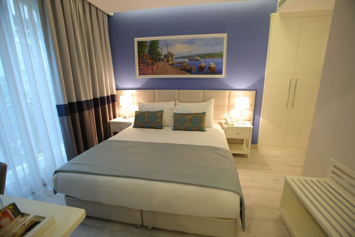 A hotel room with a large bed, two bedside tables with lamps, a painting on the wall, and a wardrobe.