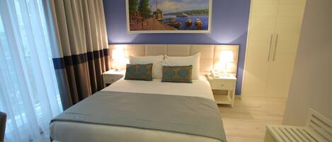 A hotel room with a large bed, two bedside tables with lamps, a painting on the wall, and a wardrobe.