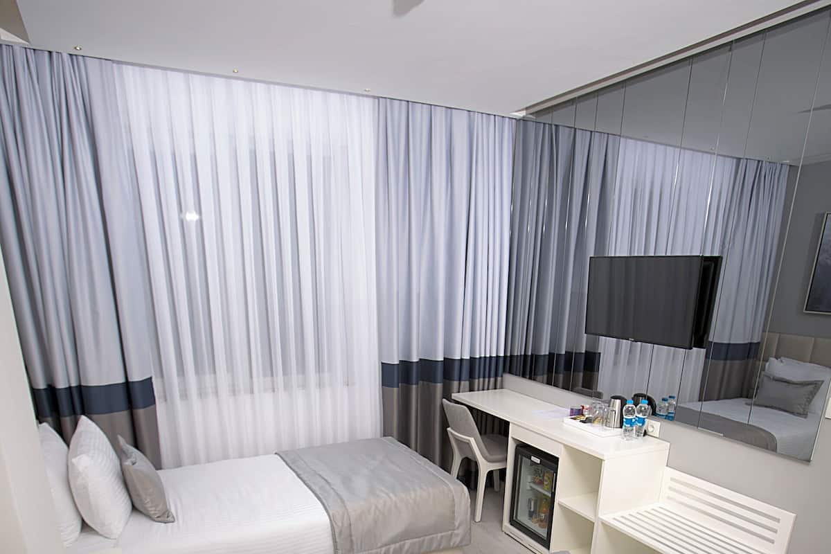 A modern hotel room with two beds, a desk, a refrigerator, and a large mirror.
