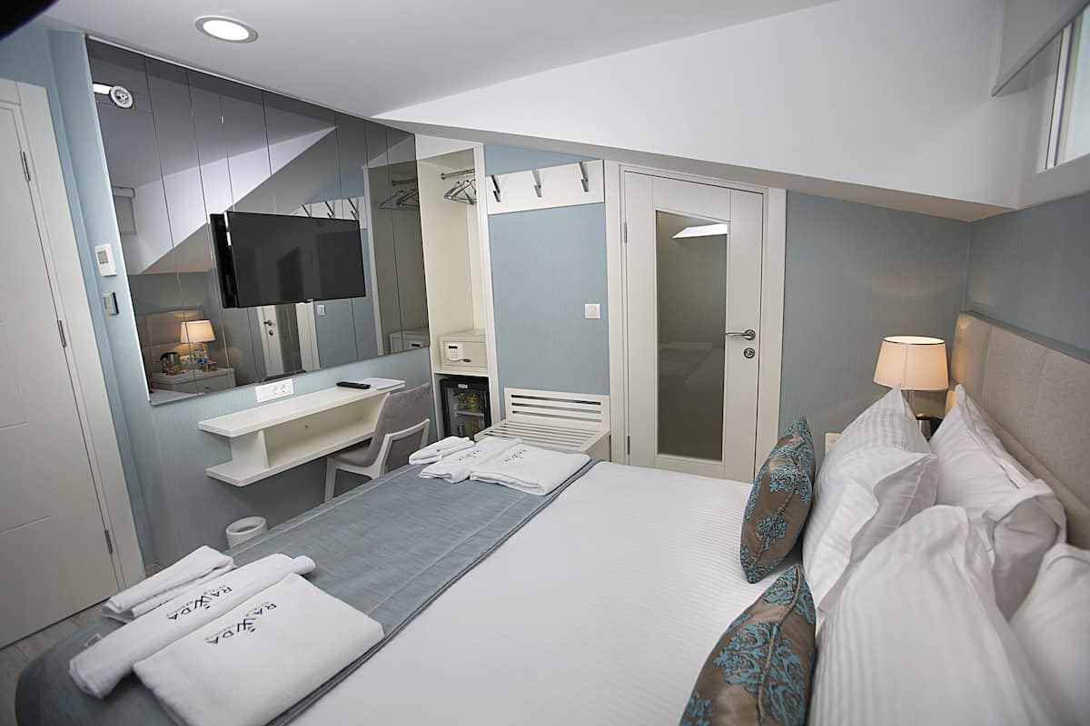 A hotel room with a bed, a desk, a chair, a TV, a mirror, a wardrobe, and a bathroom.