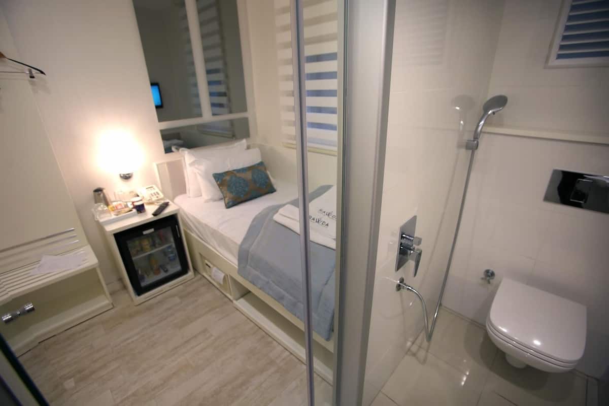 A compact hotel room with a bed, bedside table, and a small cabinet.