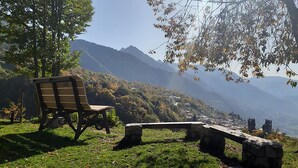 A bench and stone seating area overlooking a mountainous landscape with a view of a valley and distant buildings. - B&B Castello (Cimbergo)