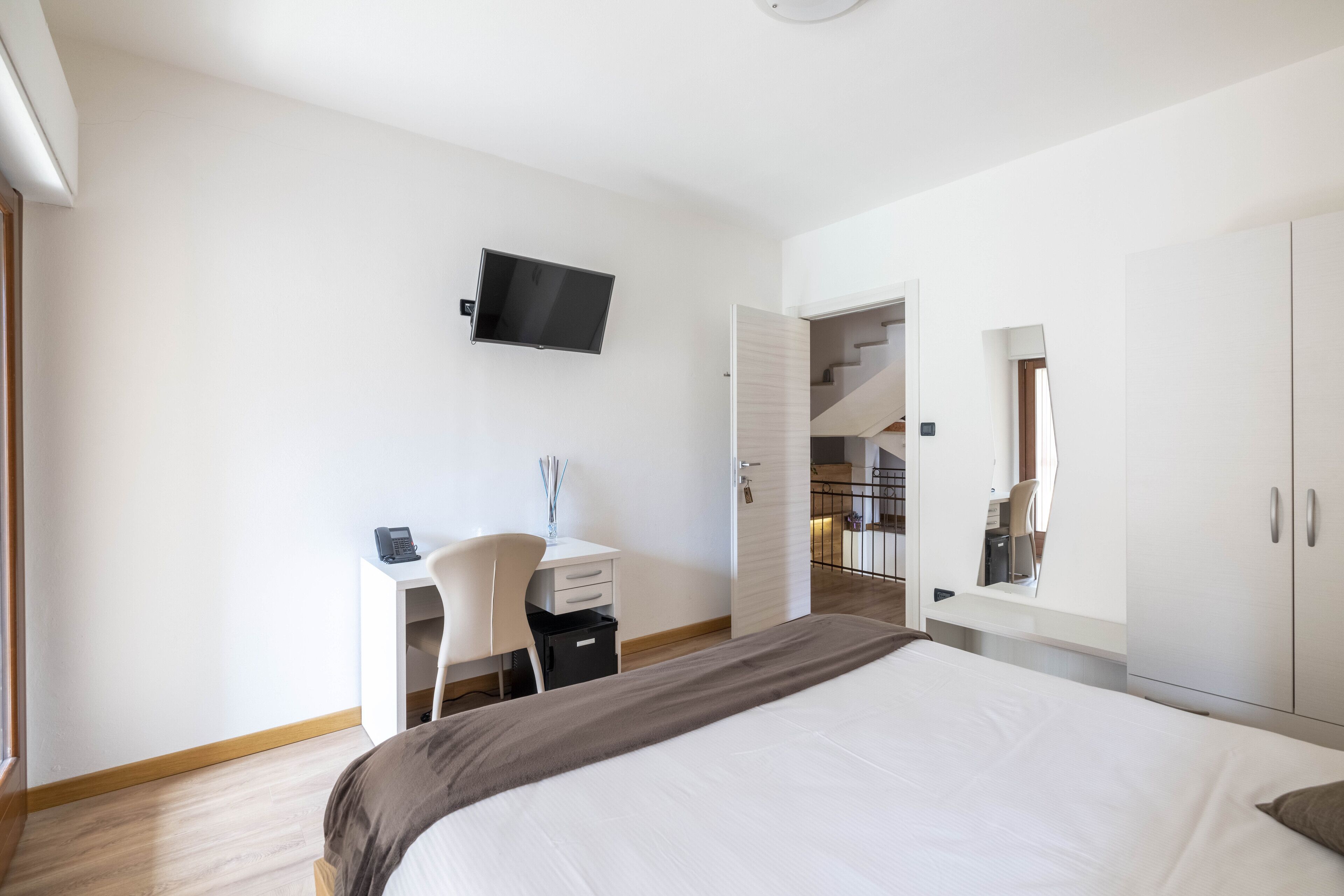 Un dormitorio moderno con una cama grande, un escritorio con silla, un televisor y un armario.