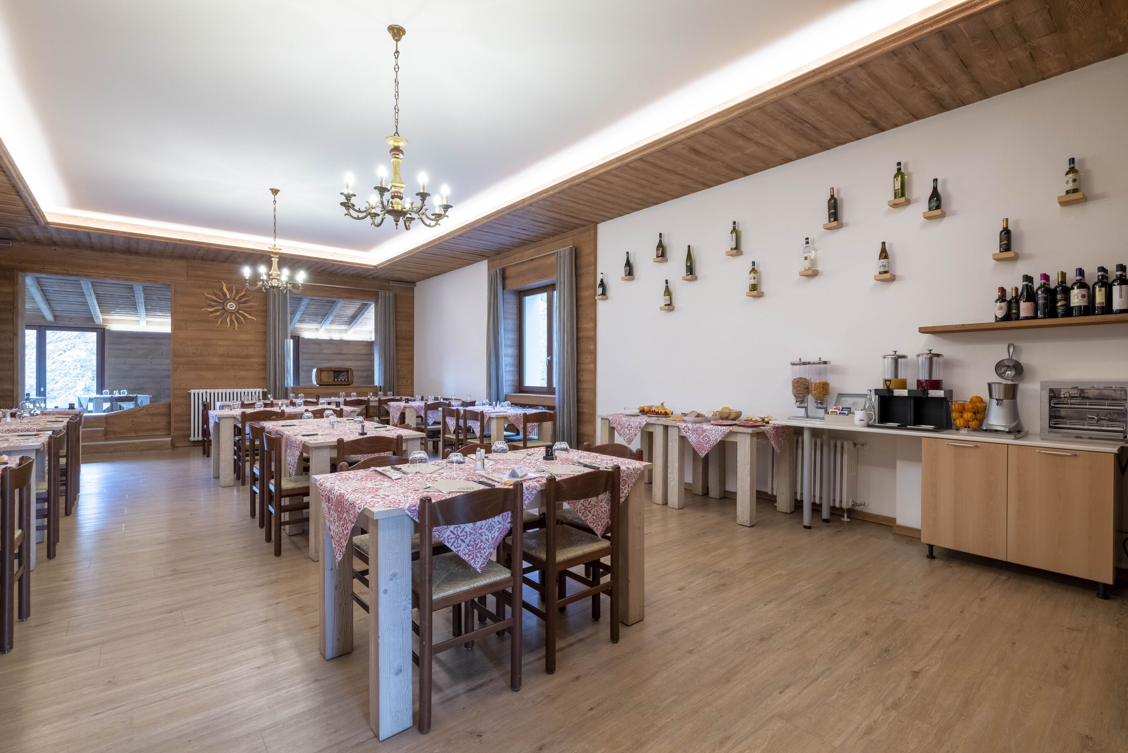 Un restaurant avec des planchers en bois, des tables recouvertes de nappes rouges et un mur entièrement composé de bouteilles de vin.