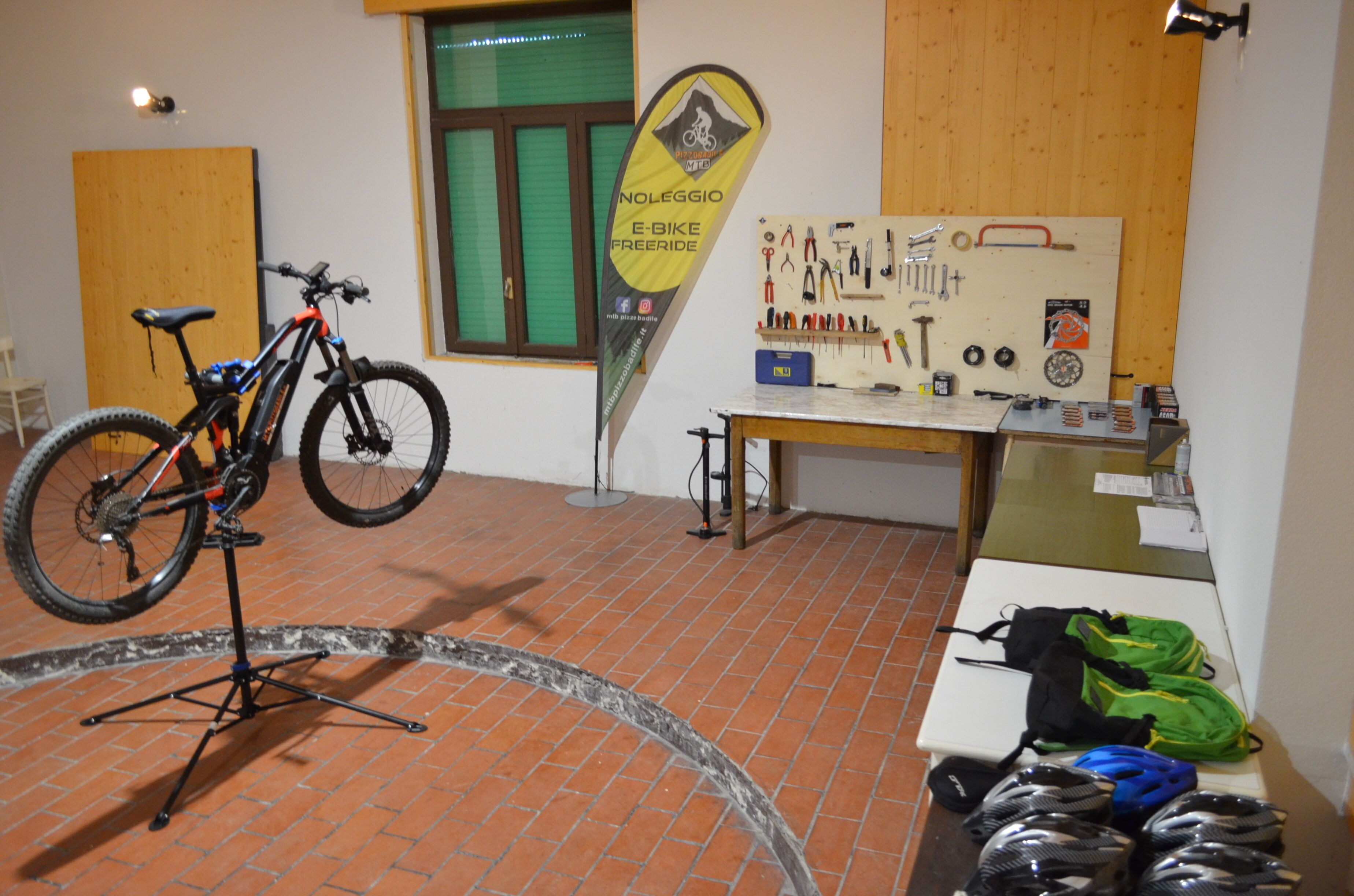 A room with a bicycle on a stand, a table with tools and a flag, and a wall with a window.