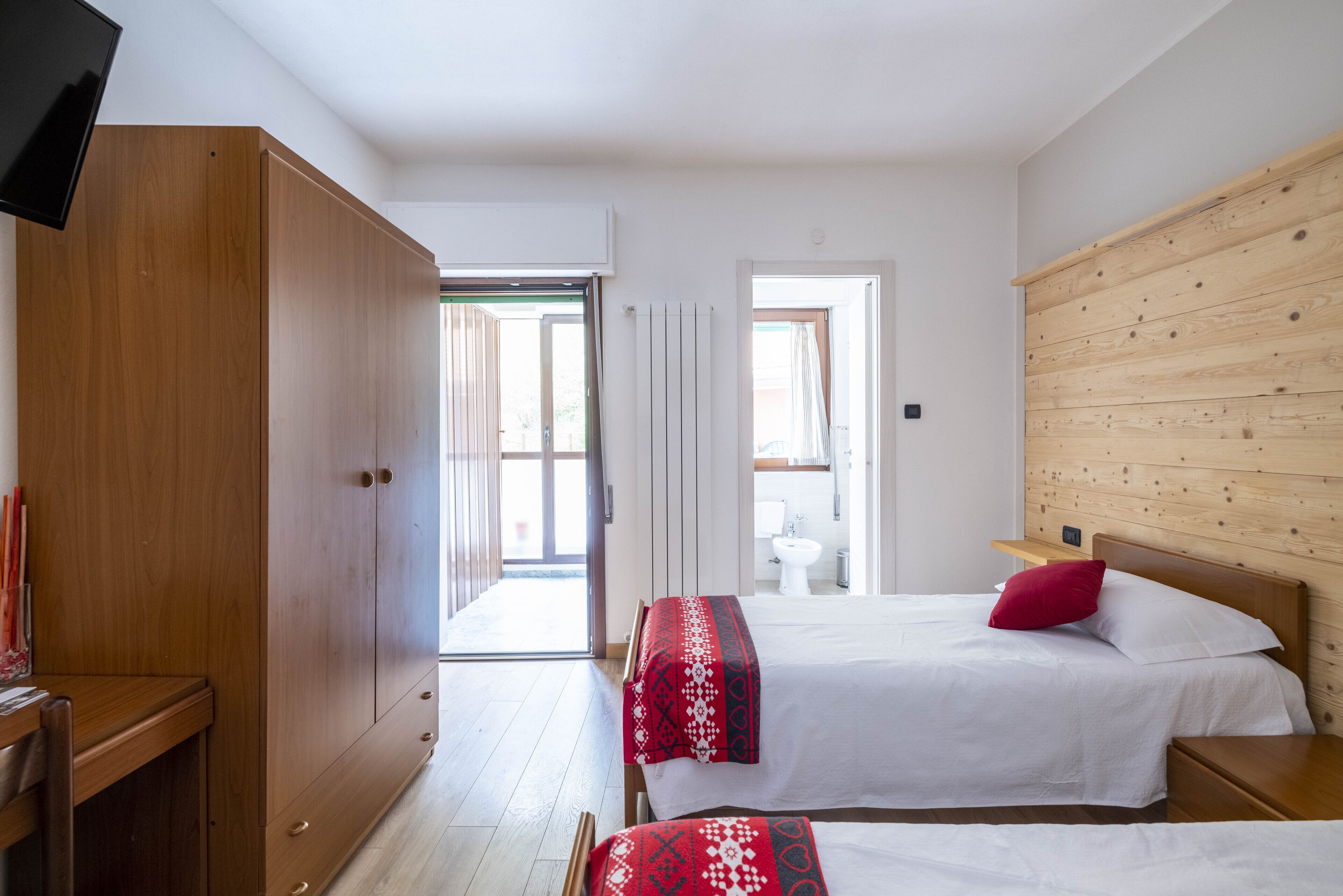 A bedroom with two beds, wooden wardrobe, and a TV.