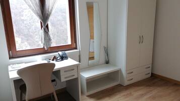 A room with a desk, chair, wardrobe, and a window with curtains.