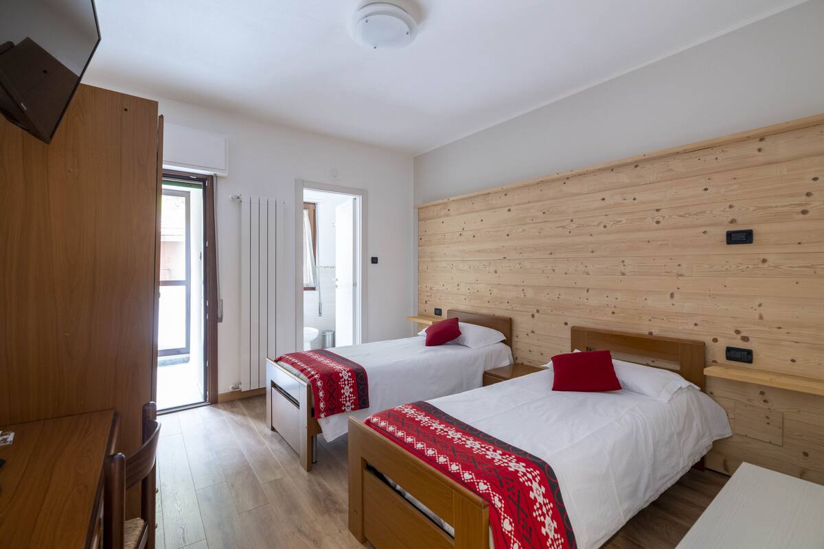 Habitació amb dos llits, amb capçaleres de fusta, un armari de fusta, una taula i una finestra.