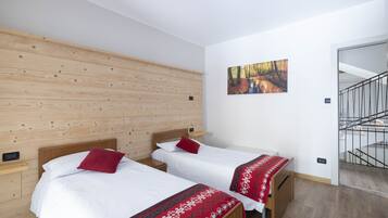 A hotel room with two beds, wooden panel walls, a painting of a forest, and a staircase.