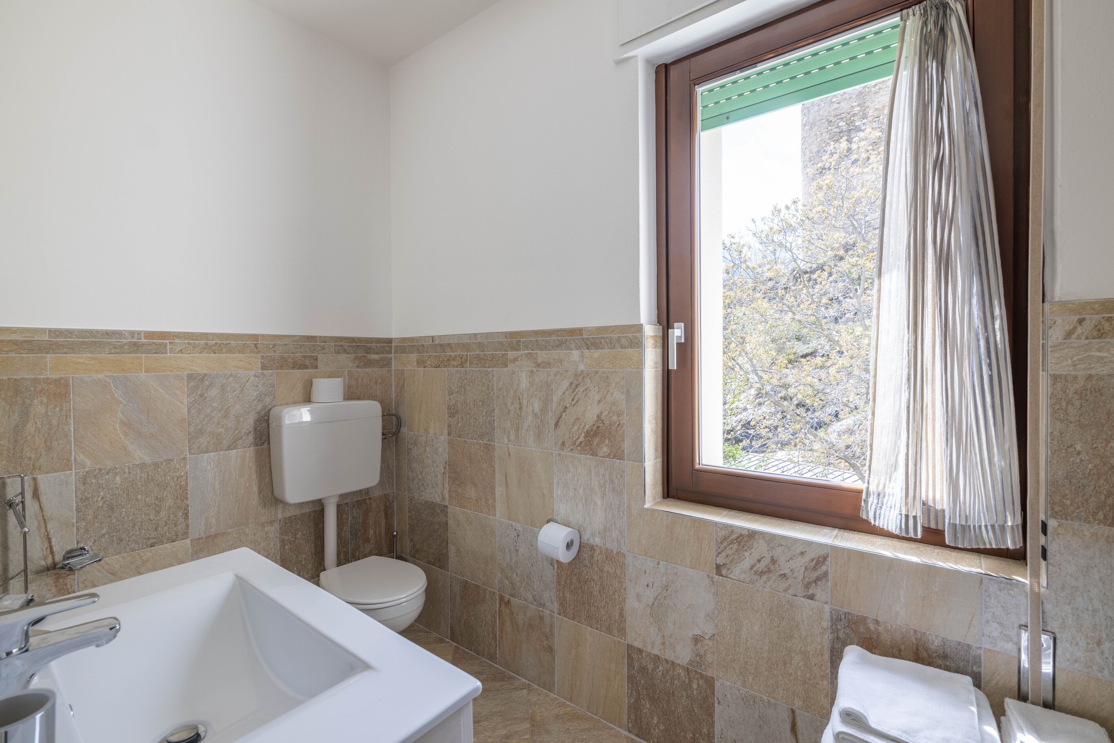 A bathroom with a bathtub, toilet, and a window with curtains.