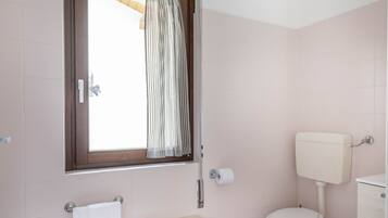 A bathroom with a window, a toilet, a sink, and a small wooden stool.