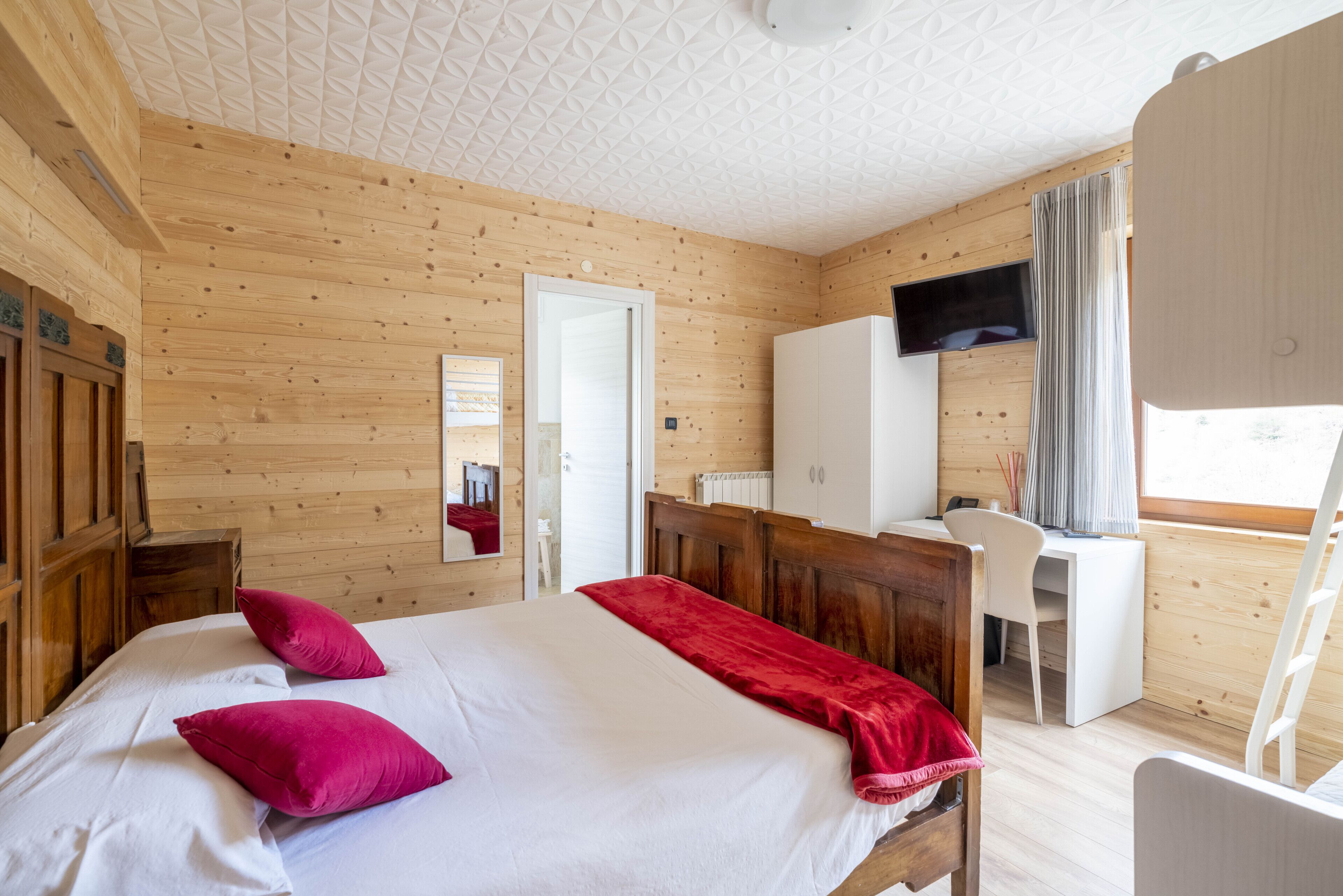 A wooden-paneled room with a bed, a desk, and a television.