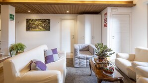 A modern living room with a wooden ceiling, a white sofa, a grey armchair, and a coffee table with plants. - B&B Castello (Cimbergo)