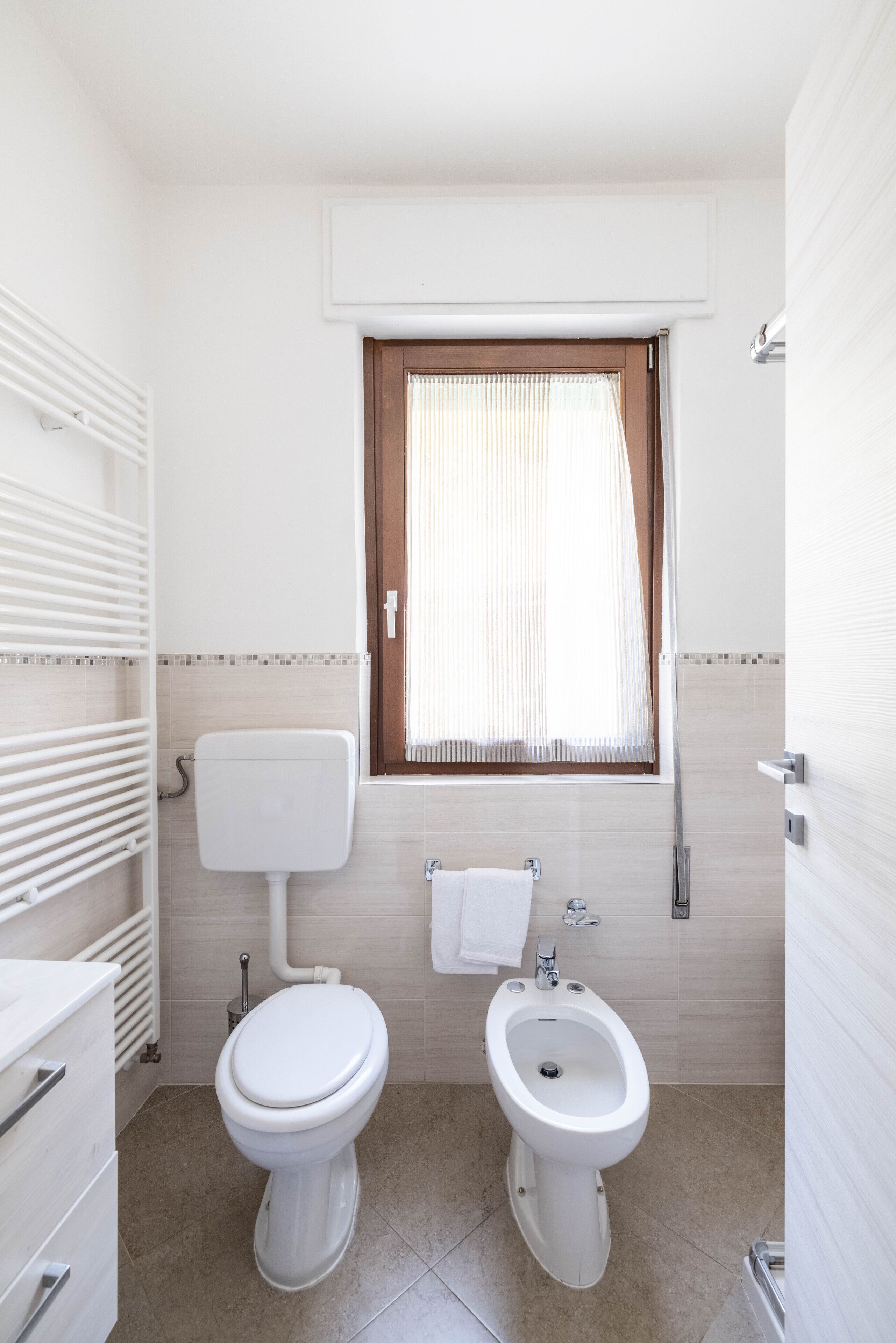 A bathroom with a toilet, bidet, and a window with curtains.