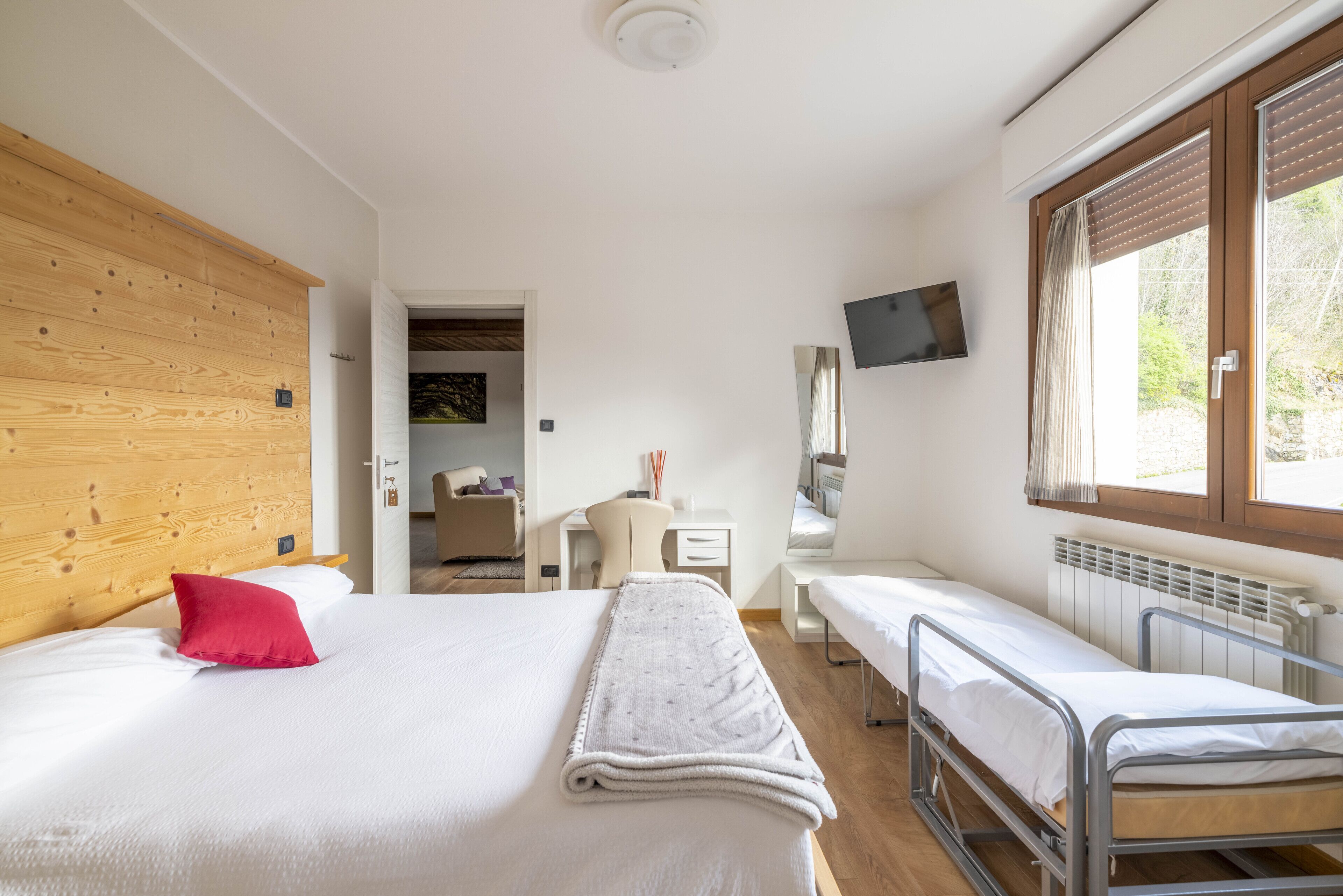 Una habitación con una cama grande, una cama más pequeña, un escritorio, una silla y un televisor en la pared.