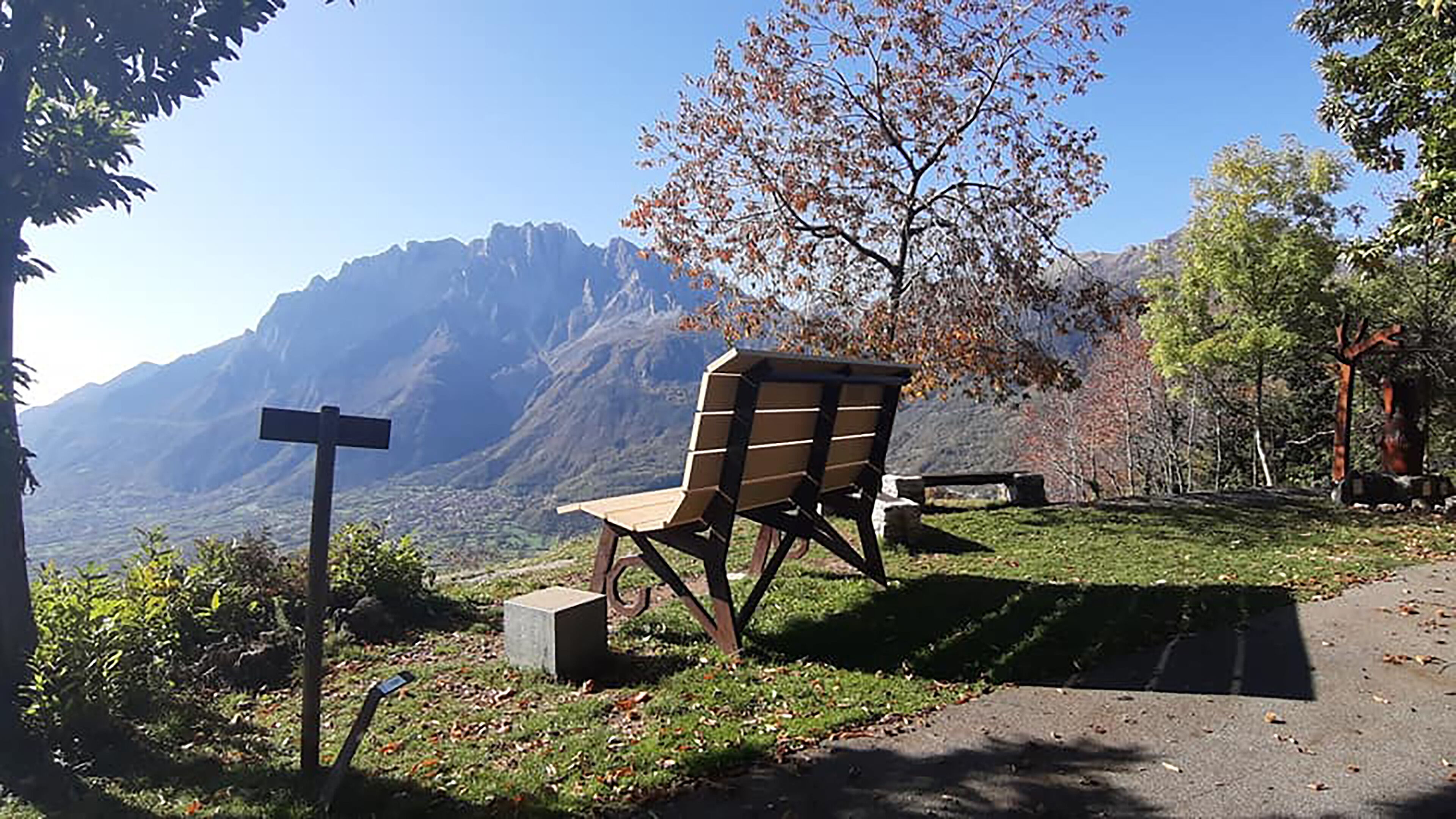 Un banc avec vue sur la montagne, un panneau indicateur et un sentier dallé.