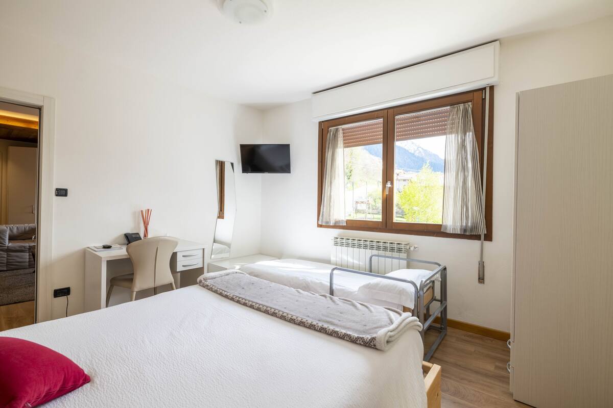 Habitació d'hotel amb llit, escriptori, cadira, televisió i finestra amb cortines.
