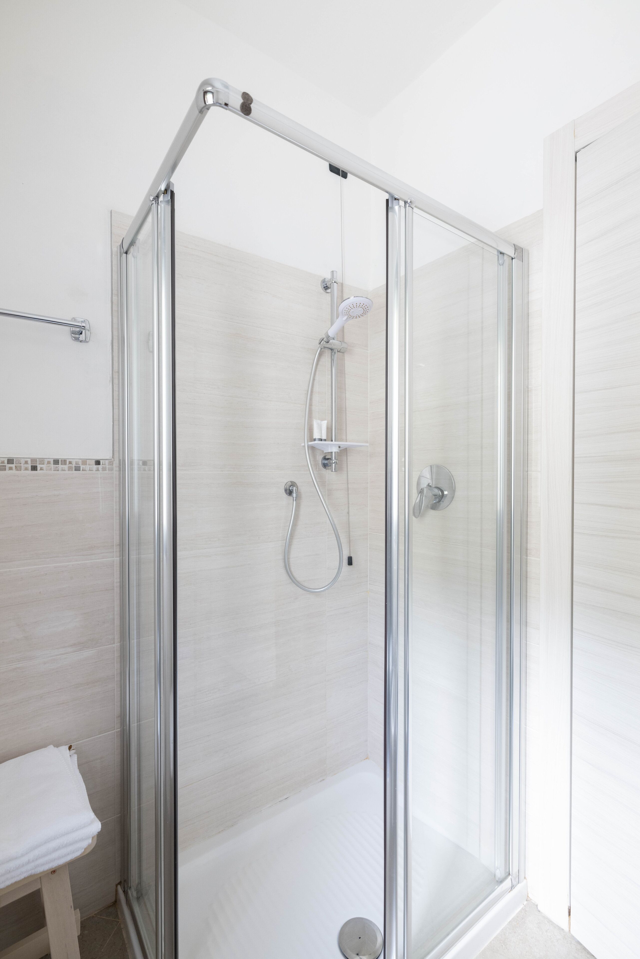Una cabina doccia in vetro con soffione a mano e rubinetto a parete.