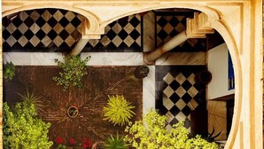 An arched doorway with a checkered floor pattern, surrounded by various plants and a small red flower arrangement. - Casa Del Regidor (El Puerto de Santa Maria)