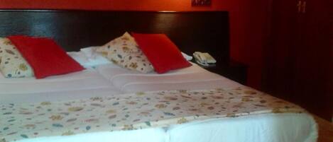 Cama doble con ropa de cama blanca y almohadas rojas, una mesita de noche con lámpara y una pared roja.