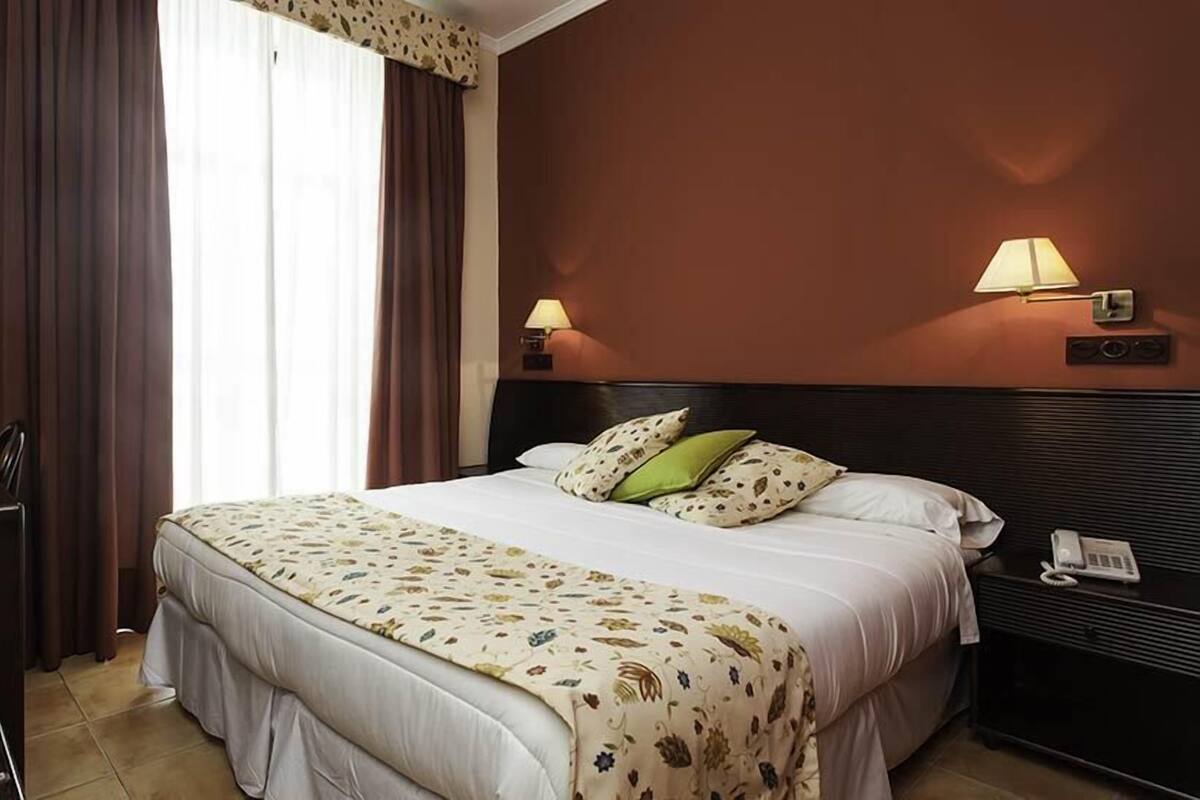 Ein Hotelzimmer mit einem Bett, einem Schreibtisch mit Computer, einem Telefon und zwei Wandlampen.