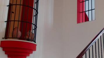 Una escalera con barandilla de madera y balaustres negros, que conduce a un rellano con una ventana de marco rojo y barandilla de balcón también roja.