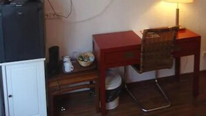 A small, compact room with a television mounted on the wall, a desk with a chair, a small cabinet, and a table with a lamp. - CityMinis (Düsseldorf)