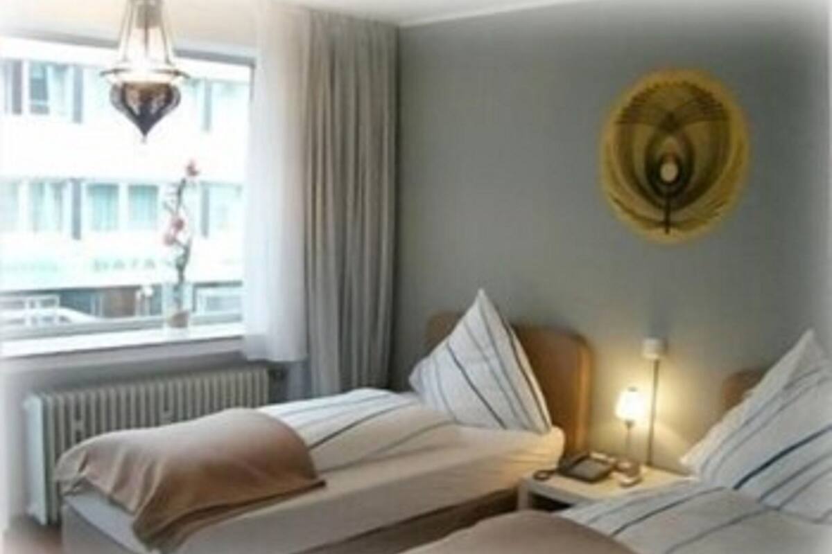 A hotel room with two beds, a window with curtains, a radiator, and a wall clock.
