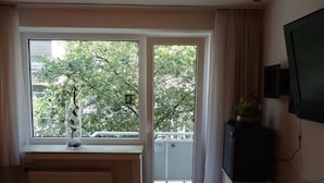 A room with a large window, a radiator below, a television on the wall, and a small cabinet. - CityMinis (Düsseldorf)