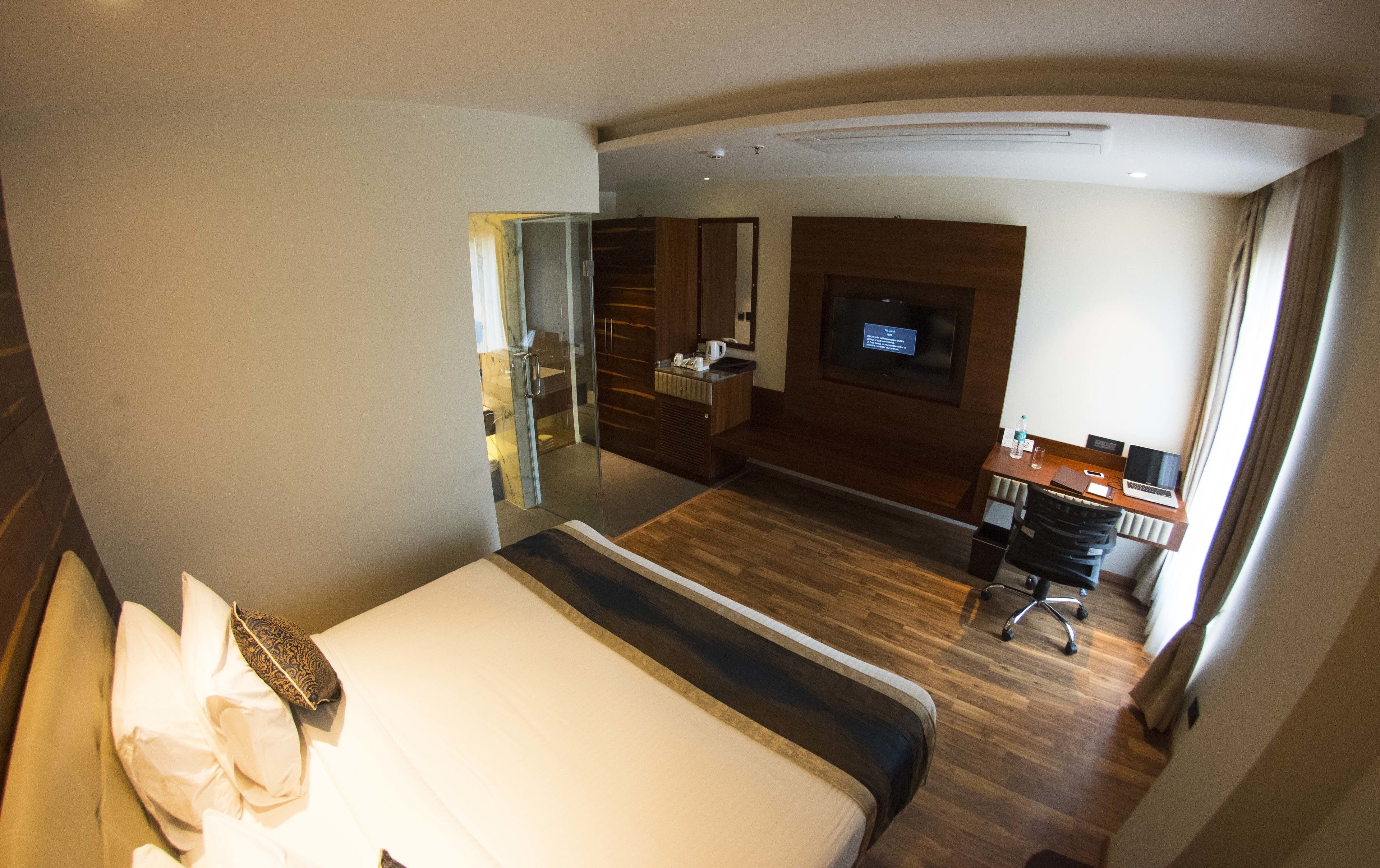 Une chambre d’hôtel avec un lit, un bureau avec un ordinateur portable, une télévision et une salle de bain visible à travers une porte en verre.