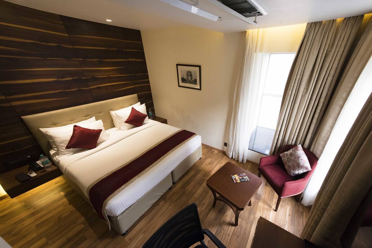 A hotel room with a large bed, a desk, a chair, and a view of the outside.