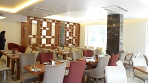 Een modern restaurant met diverse zitmogelijkheden, waaronder tafels en hoekbanken. Er is een decoratieve wand met een geometrisch patroon en een grote pilaar met een marmerachtige textuur.