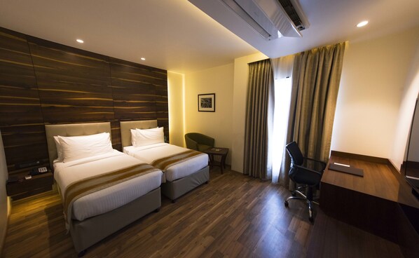 A hotel room with two beds, a desk, a chair, and a small table.