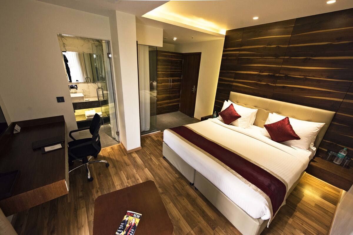 A modern hotel room with a large bed, a desk, and a glass-enclosed bathroom.