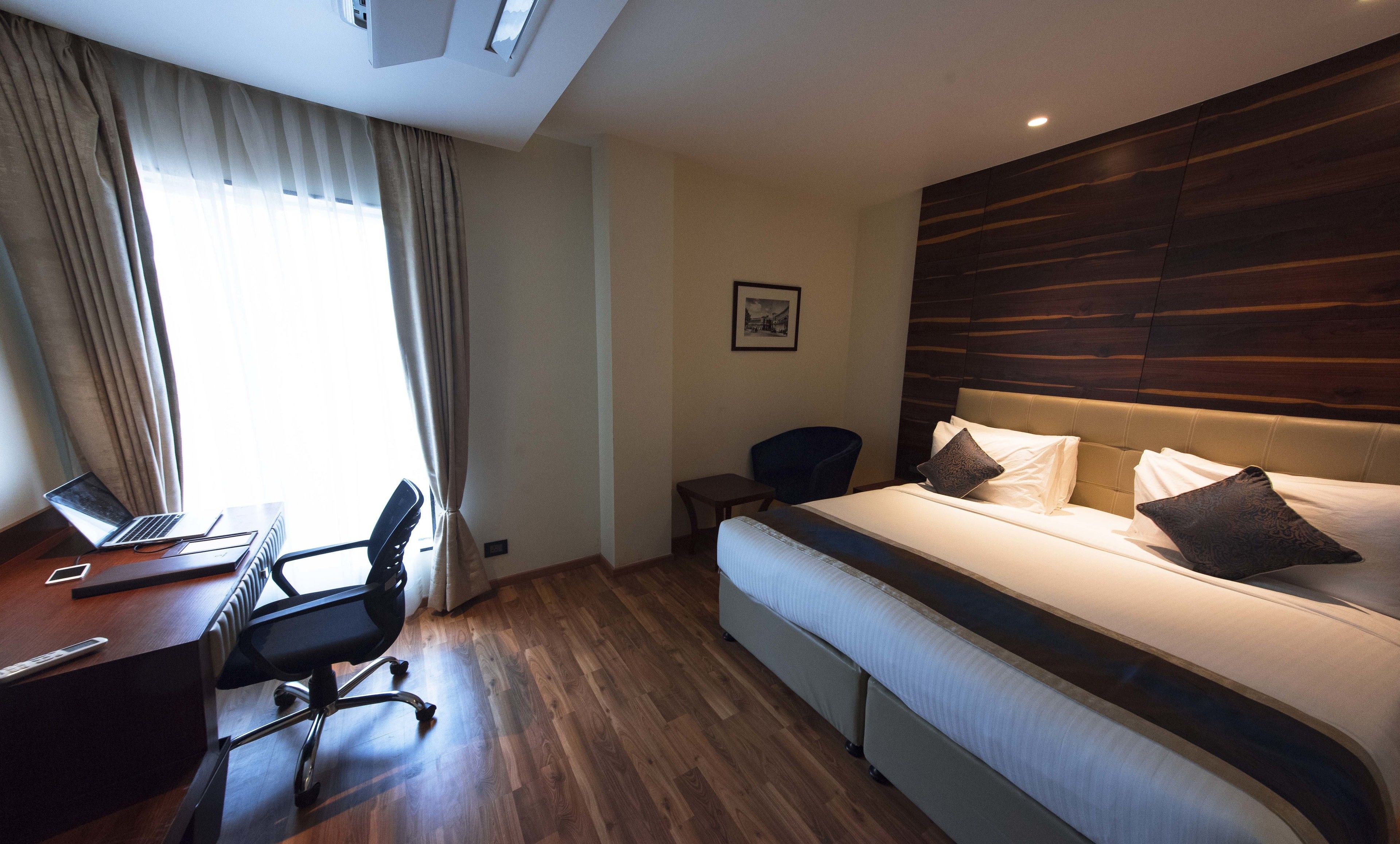 A hotel room with a bed, a desk with a laptop, a chair, and a window with curtains.