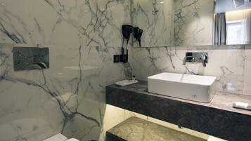 A modern bathroom with a marble wall, a white toilet, a sink, and a mirror.