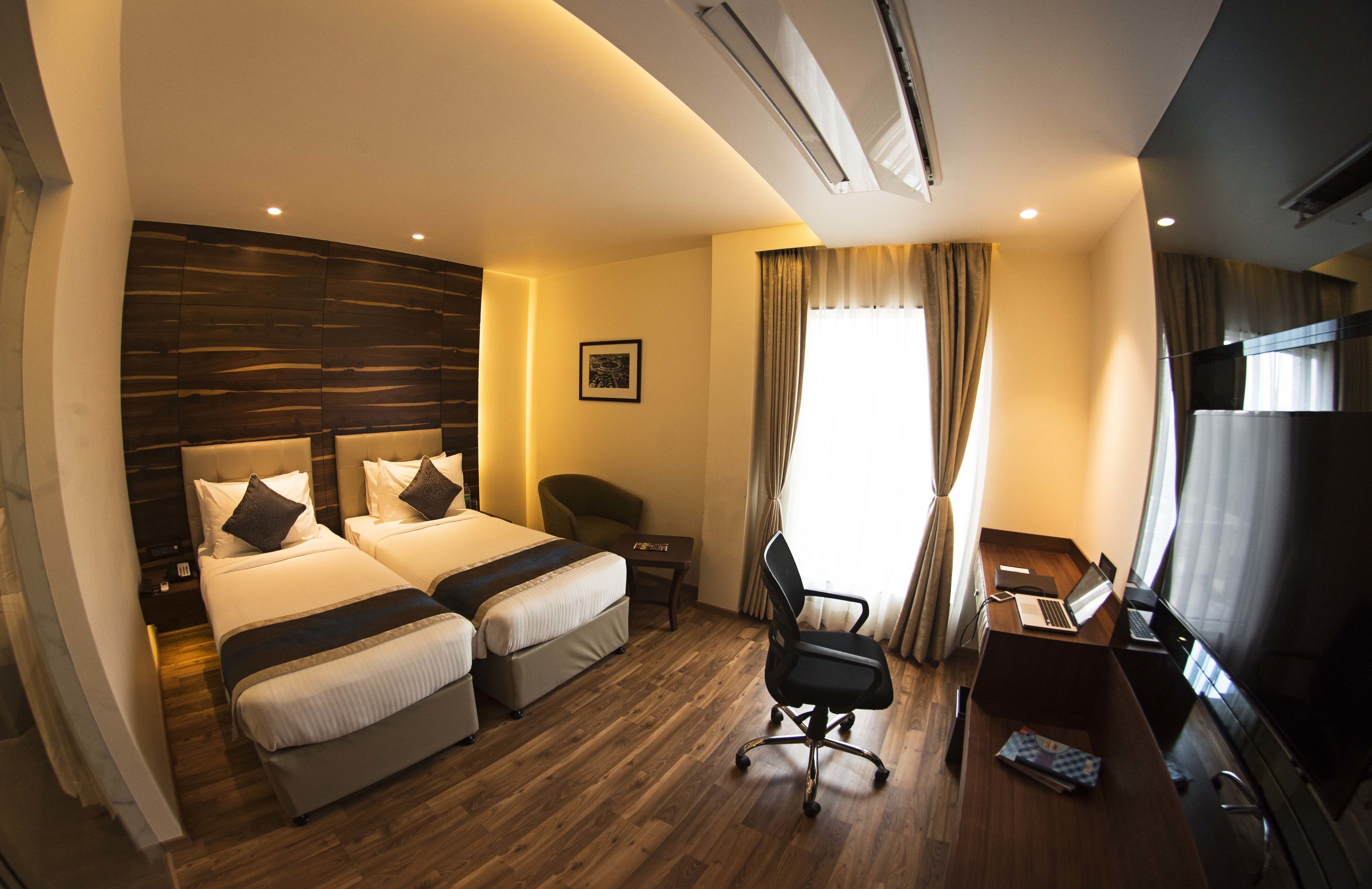 A hotel room with two beds, a desk with a laptop, a chair, and a TV.