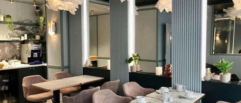 A modern dining area with a long table and chairs, a coffee machine, and decorative plants.
