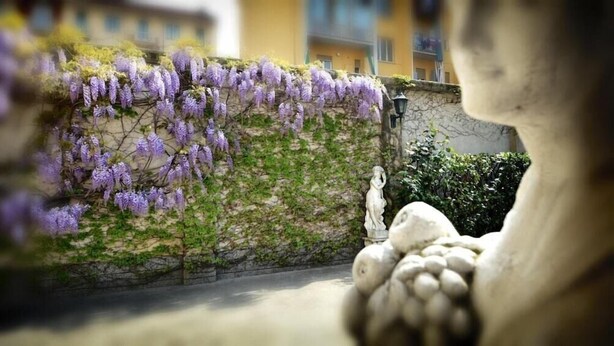 Un mur de pierre orné de fleurs violettes, une statue et un bâtiment en arrière-plan.