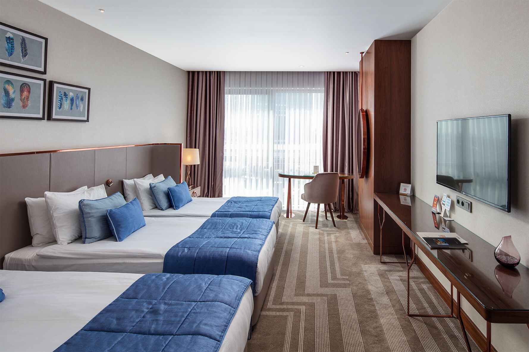 A hotel room with two beds, a desk, a chair, a TV, and a window with curtains.