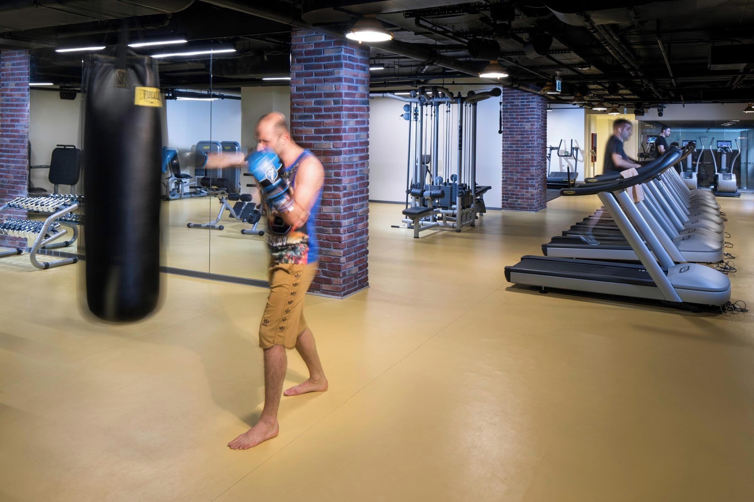 Een fitnessruimte met trainingsapparatuur, waaronder een bokszak, loopbanden en krachttoestellen.