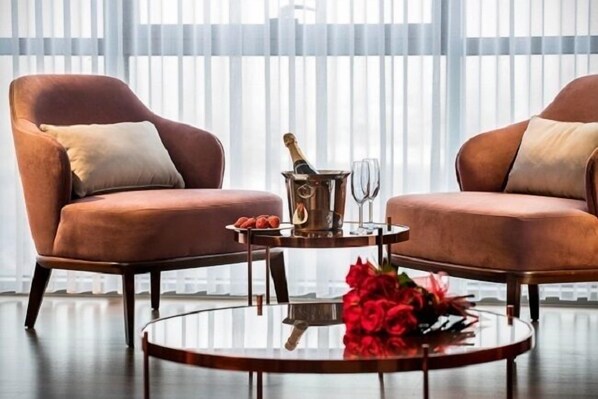 Une pièce avec deux fauteuils marron, une table basse en verre sur laquelle se trouvent une bouteille de champagne, un verre et une assiette de collations.