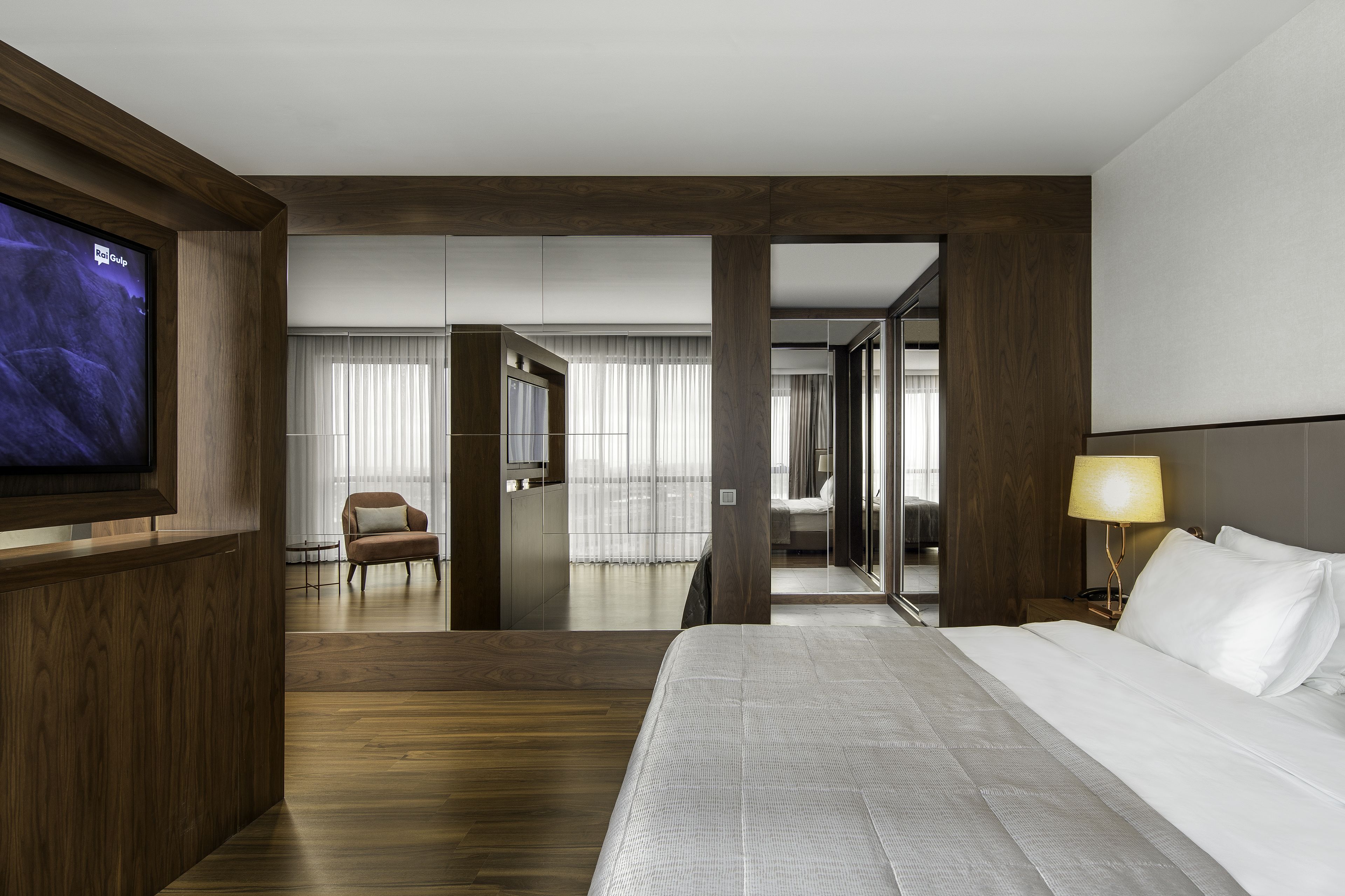 A hotel room with a large bed, a TV mounted on the wall, a desk, and a chair.