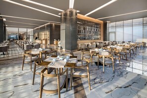 A spacious restaurant with marble flooring, wooden tables and chairs, and a modern interior design.